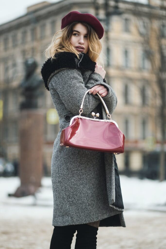 Stylish woman in winter coat and beret holding handbag outdoors.