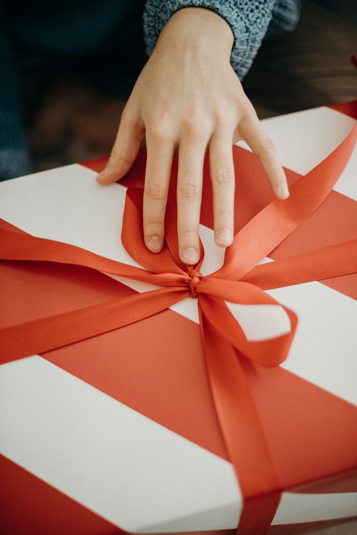 A hand unwraps a gift box with a red ribbon, symbolizing celebration and surprise.