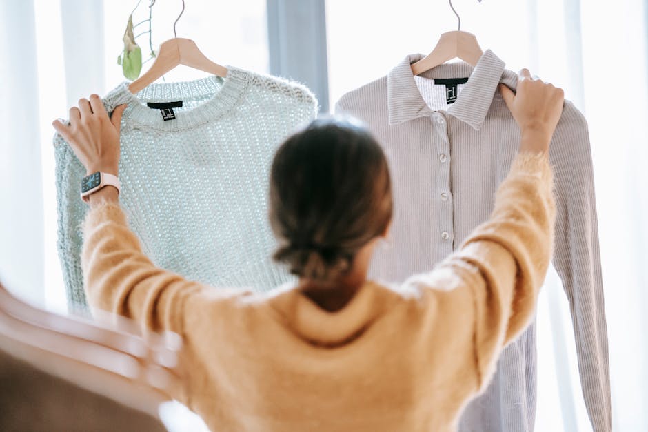 Woman deciding between two trendy sweaters in a modern boutique setting.