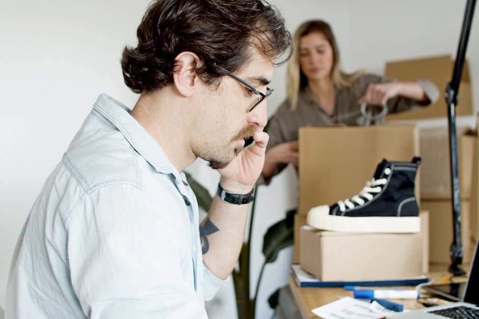 A businessman on a phone call while preparing an online order for shipping in a modern office.